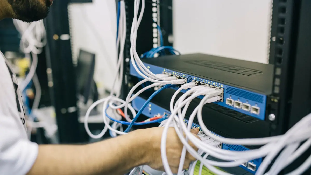 Technician patching white ethernet cables into a network switch in a comms rack