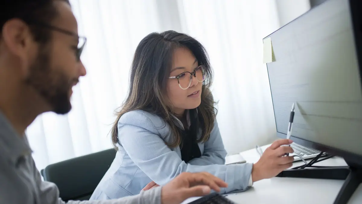 Technician beside an office worker pointing at her desktop monitor while sorting a computer issue